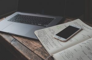 An iphone on top of a notebook next to a laptop